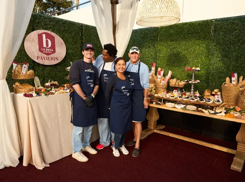 Three people in navy aprons stand at a dessert table in a decorated event booth.