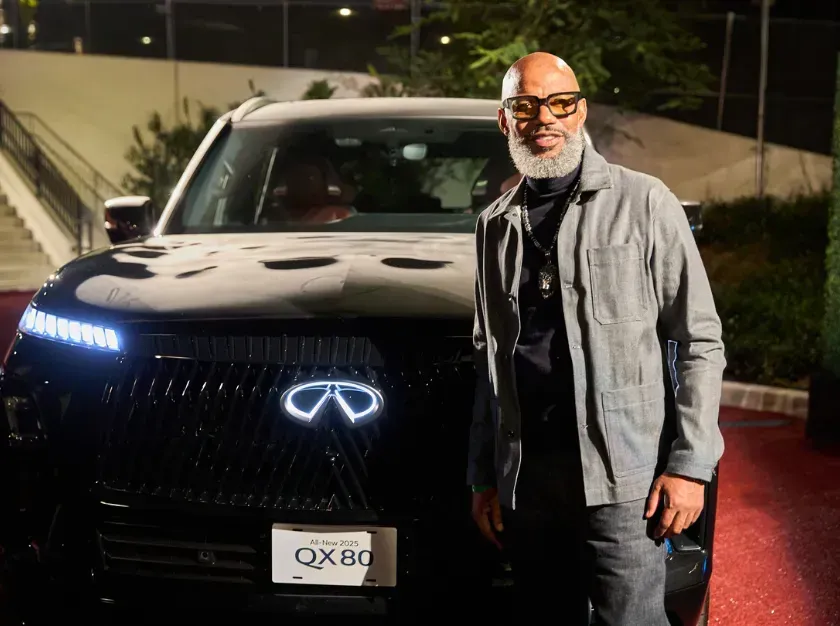 Man posing beside a black Infiniti SUV at night with headlights on