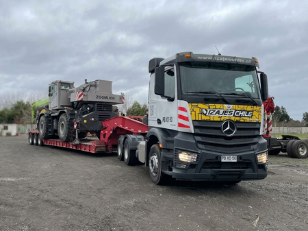 Grúa de remolque negra de servicio pesado transportando maquinaria en un remolque de plataforma baja rojo.