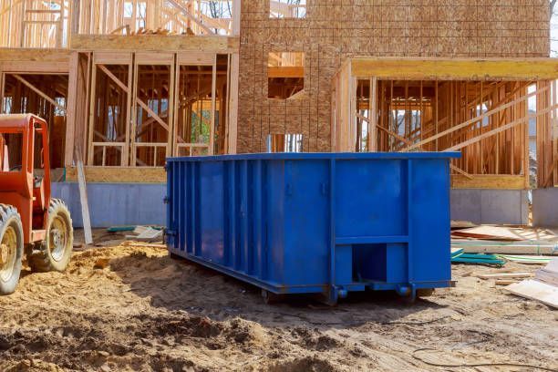 Blue dumpster at construction site, with partially framed house in the background.
