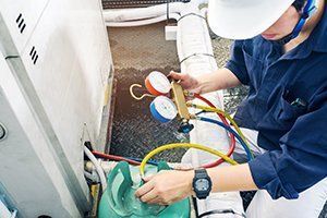 A man is working on a refrigerator with a vacuum gauge.
