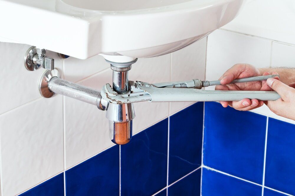 A Person is Fixing a Sink With a Wrench — MacKenzie Plumbing In West Mackay, QLD