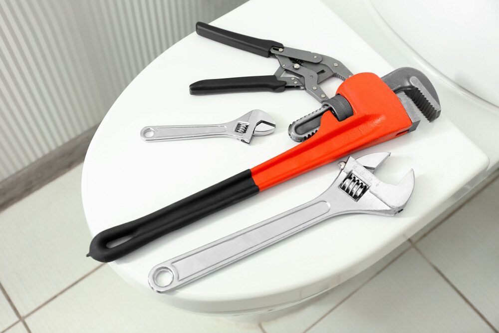 A Toilet Seat With a Wrench and Pliers on It — MacKenzie Plumbing In Northern Beaches, NSW