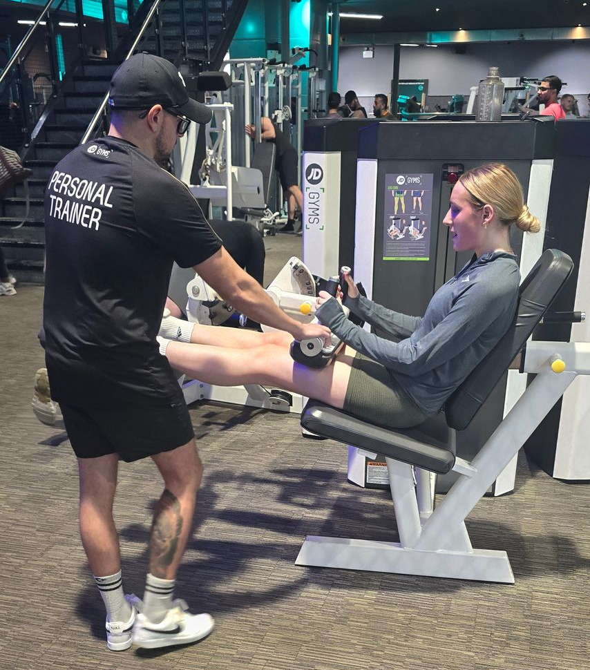 Personal trainer assisting a person on a leg extension machine in a gym.