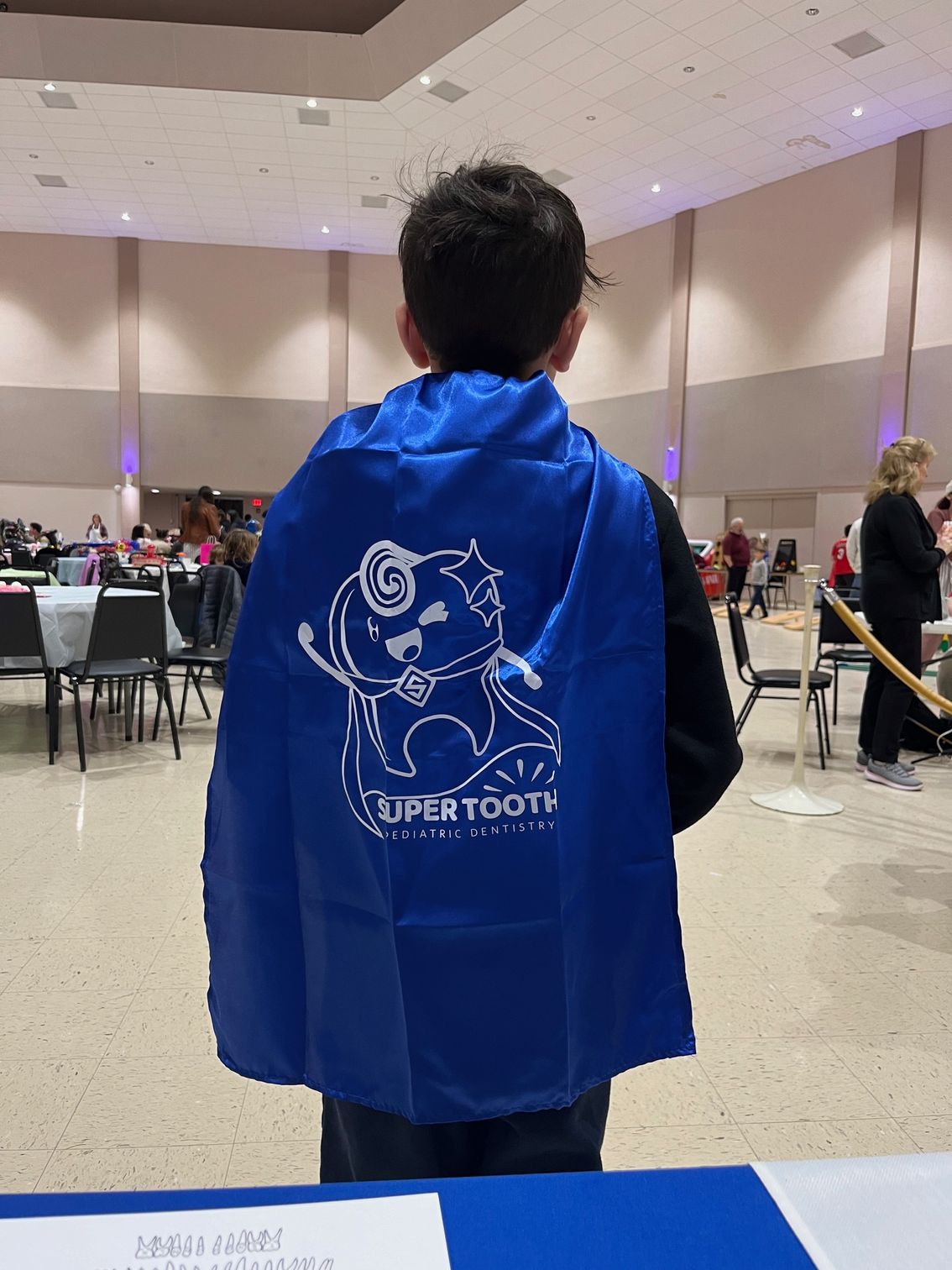 A young boy wearing a blue cape with an elephant on it.