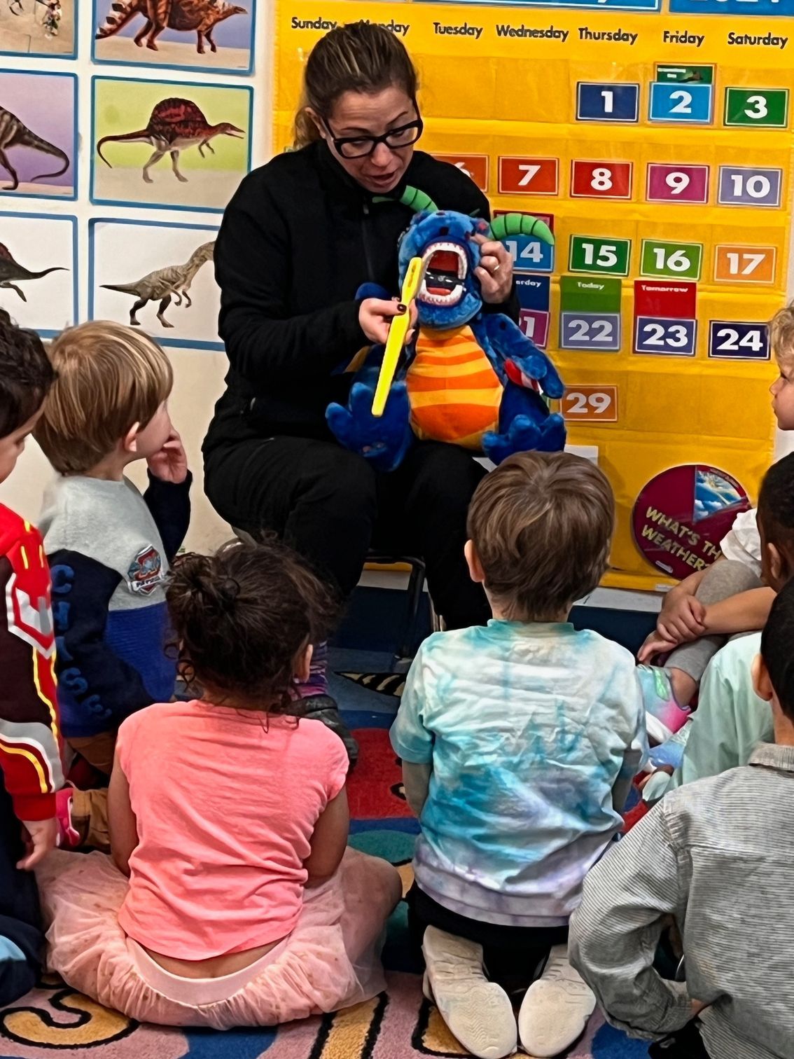 A woman is teaching a group of children how to brush their teeth.