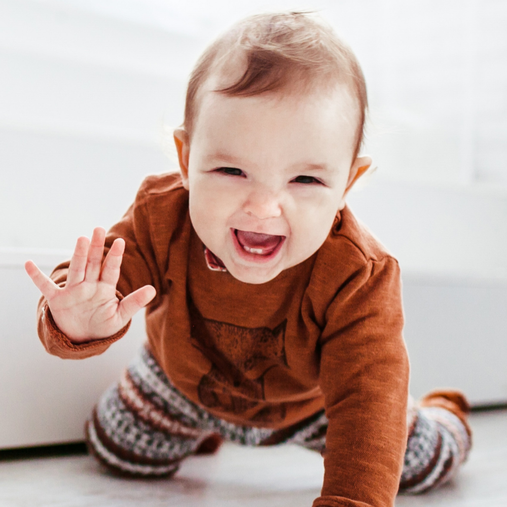 Baby wearing a brown sweater and pants, crawling towards the camera on a white floor