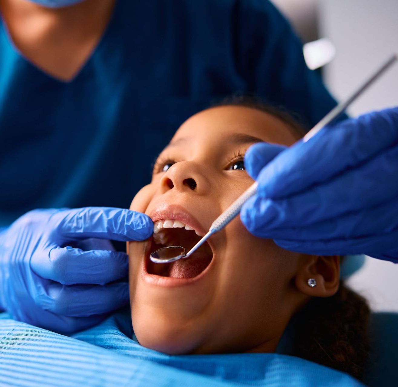 Experienced dentist for children in East Norriton, PA. A little girl is getting her teeth examined by a dentist.