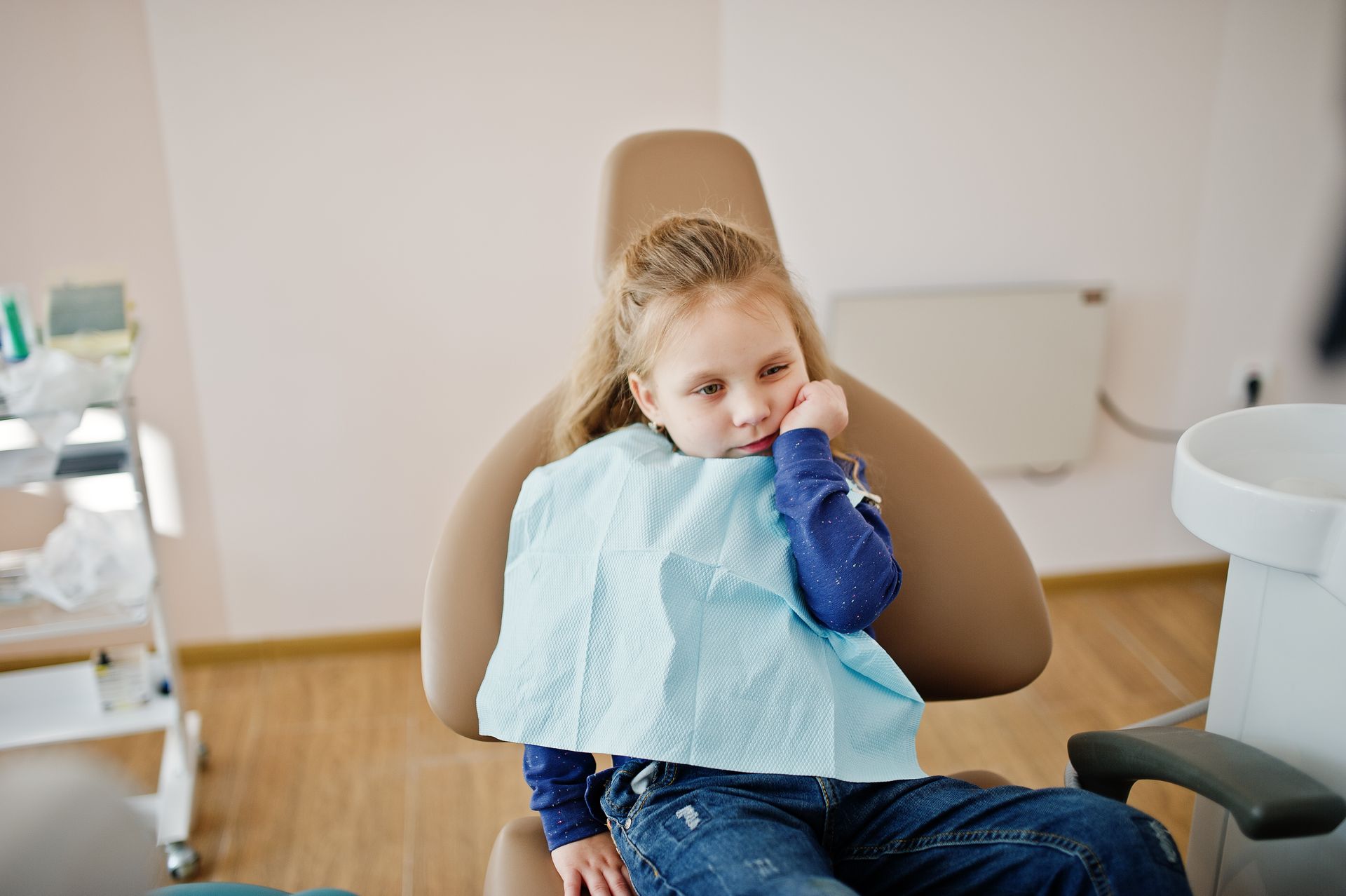 A little girl is sitting in a dental chair with a towel around her neck.