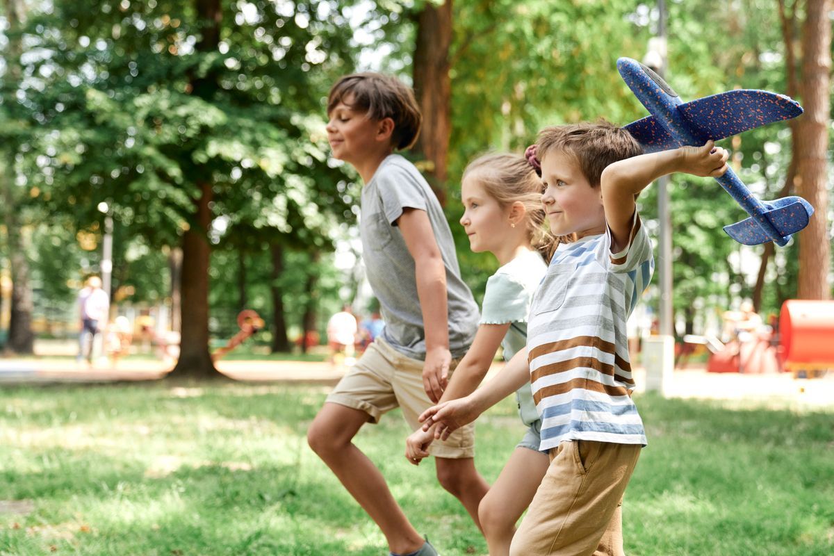 Three children running through a park, one holding a blue toy airplane