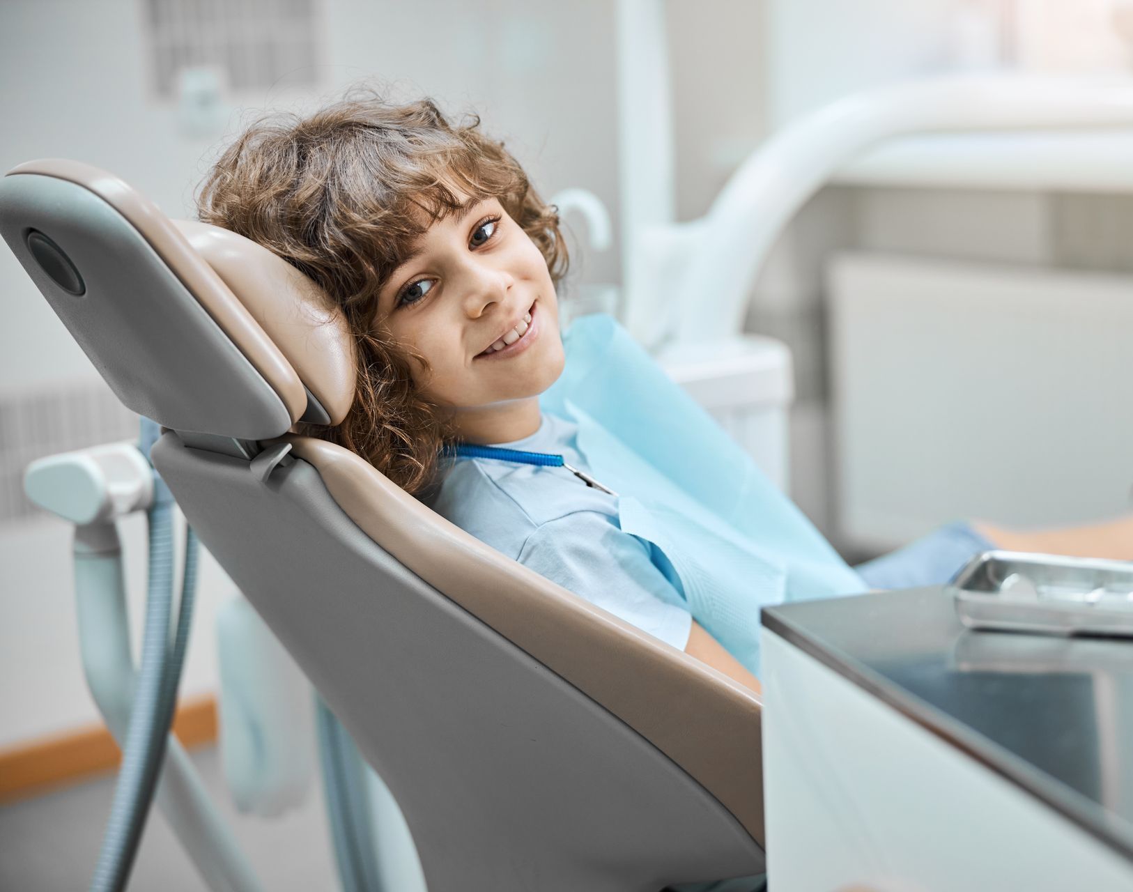 A young boy is sitting in a dental chair and smiling.