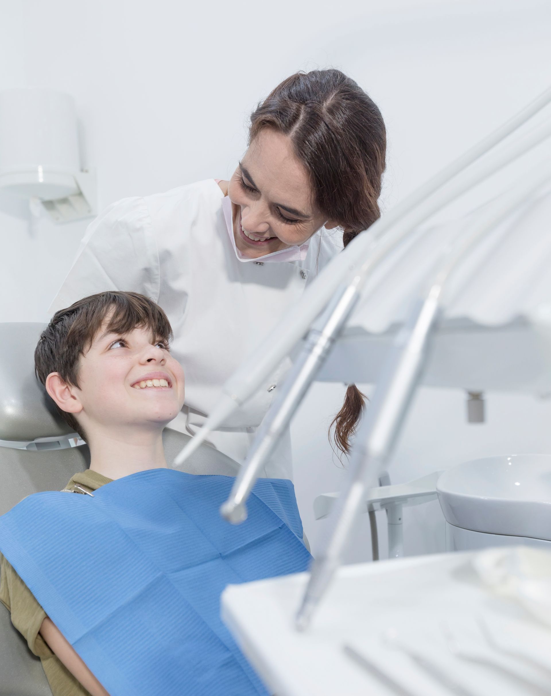 A female dentist is talking to a young boy in a dental chair.