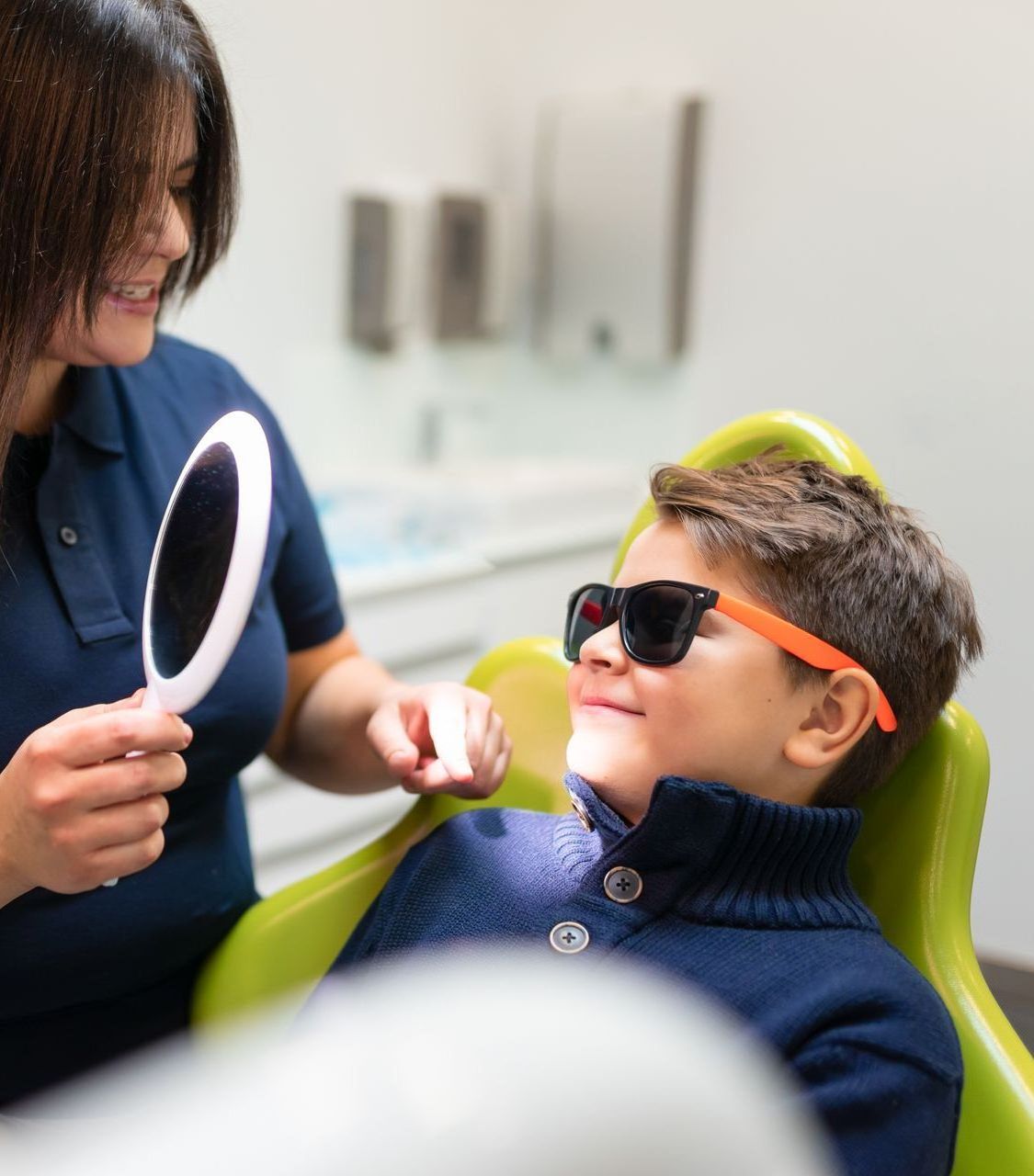 Reliable kids' dentist at Swede Square, East Norriton, PA. A woman is looking at a young boy 's teeth in a mirror.