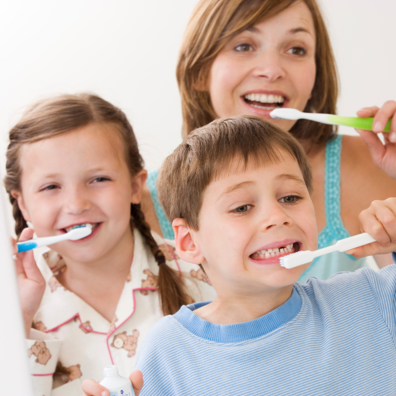 Woman and two children holding and using toothbrushes while looking into a mirror