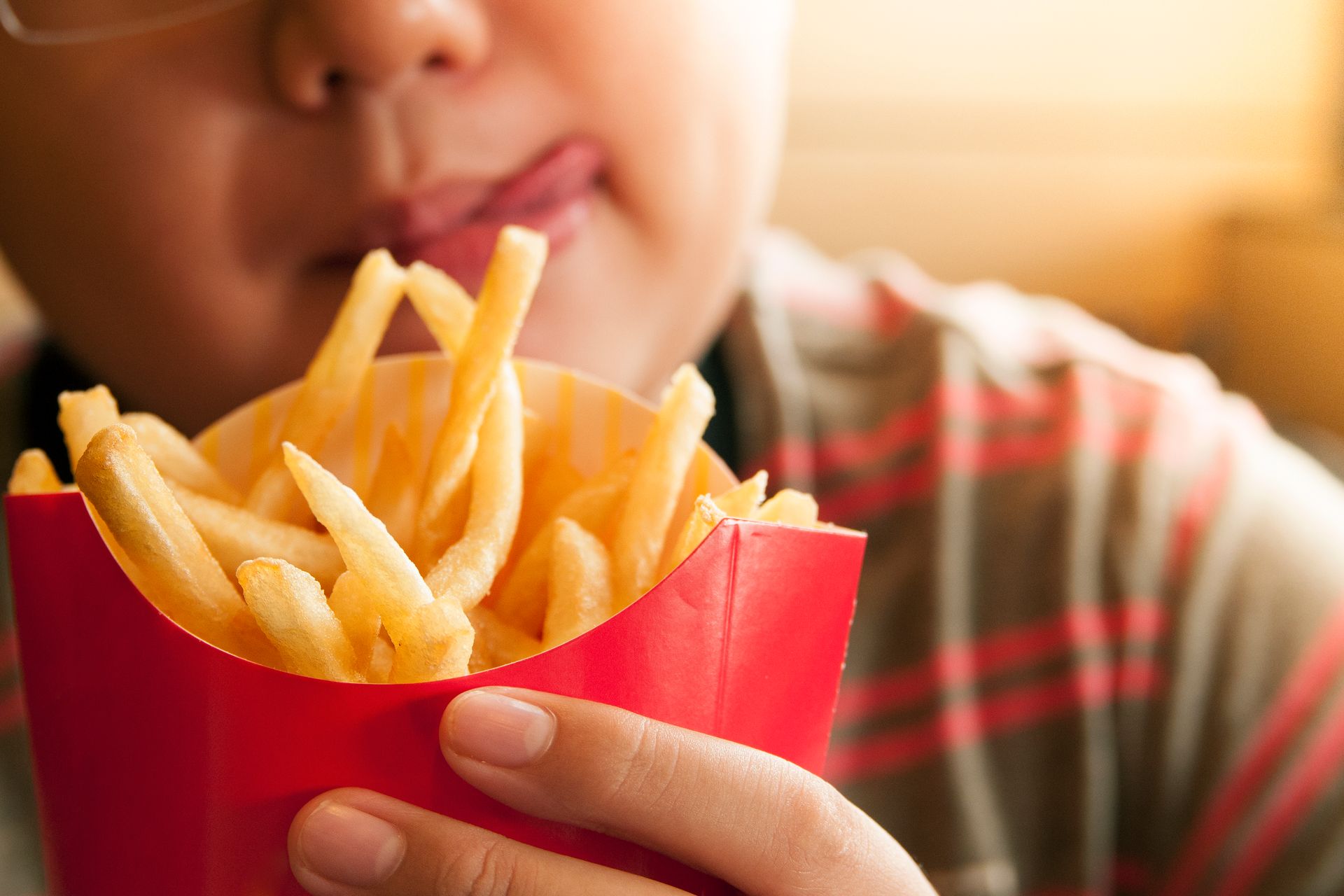 A person holds a red carton of golden French fries, licking their lips in anticipation.