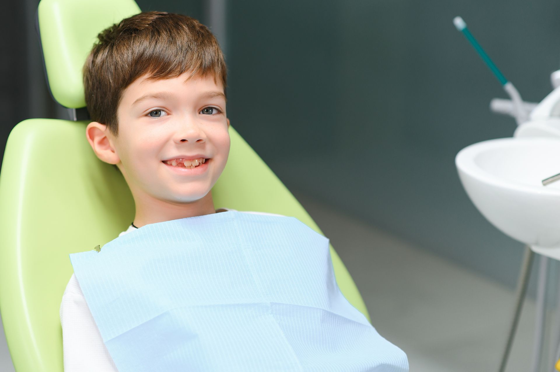 A young boy is sitting in a dental chair and smiling.