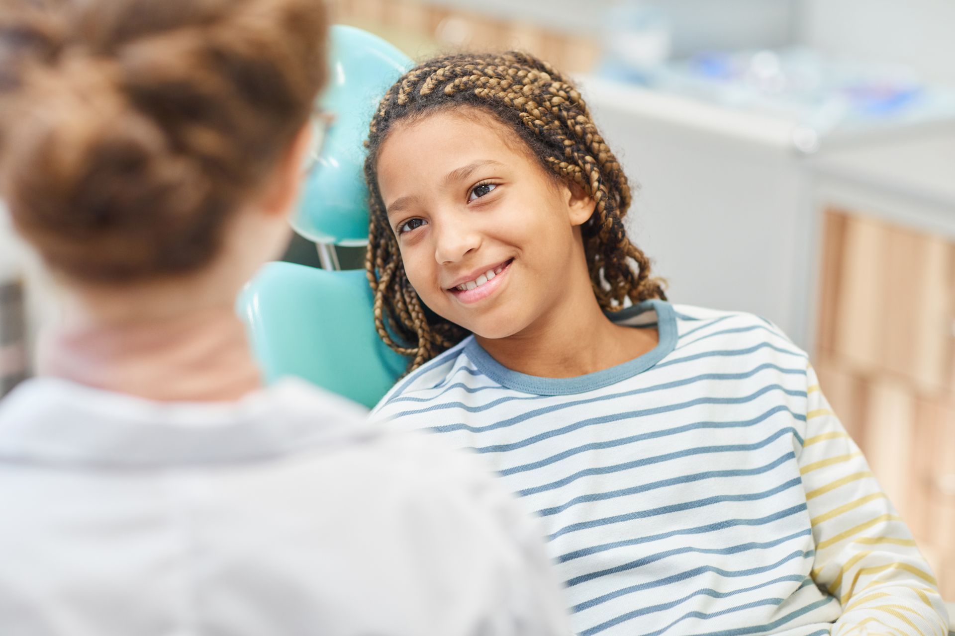 A young girl is sitting in a dental chair talking to a dentist.