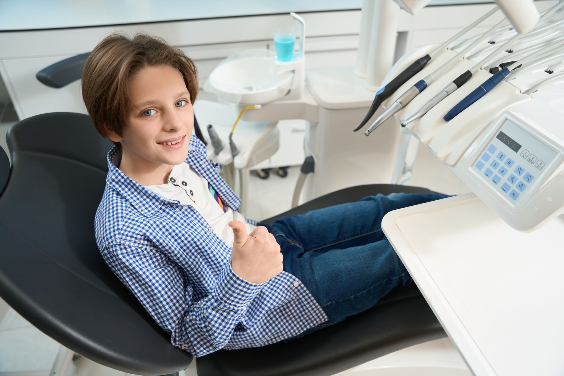A young boy is sitting in a dental chair and giving a thumbs up.