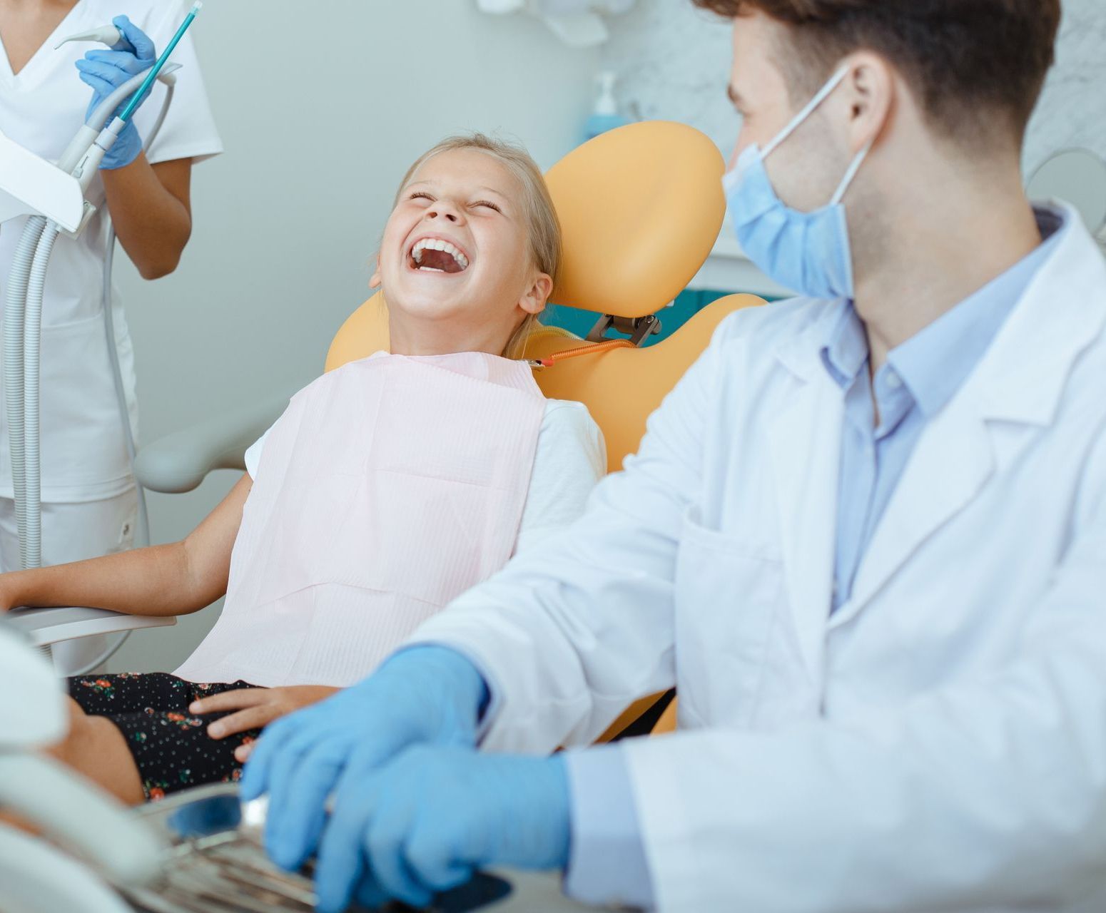 A little girl is laughing while sitting in a dental chair.