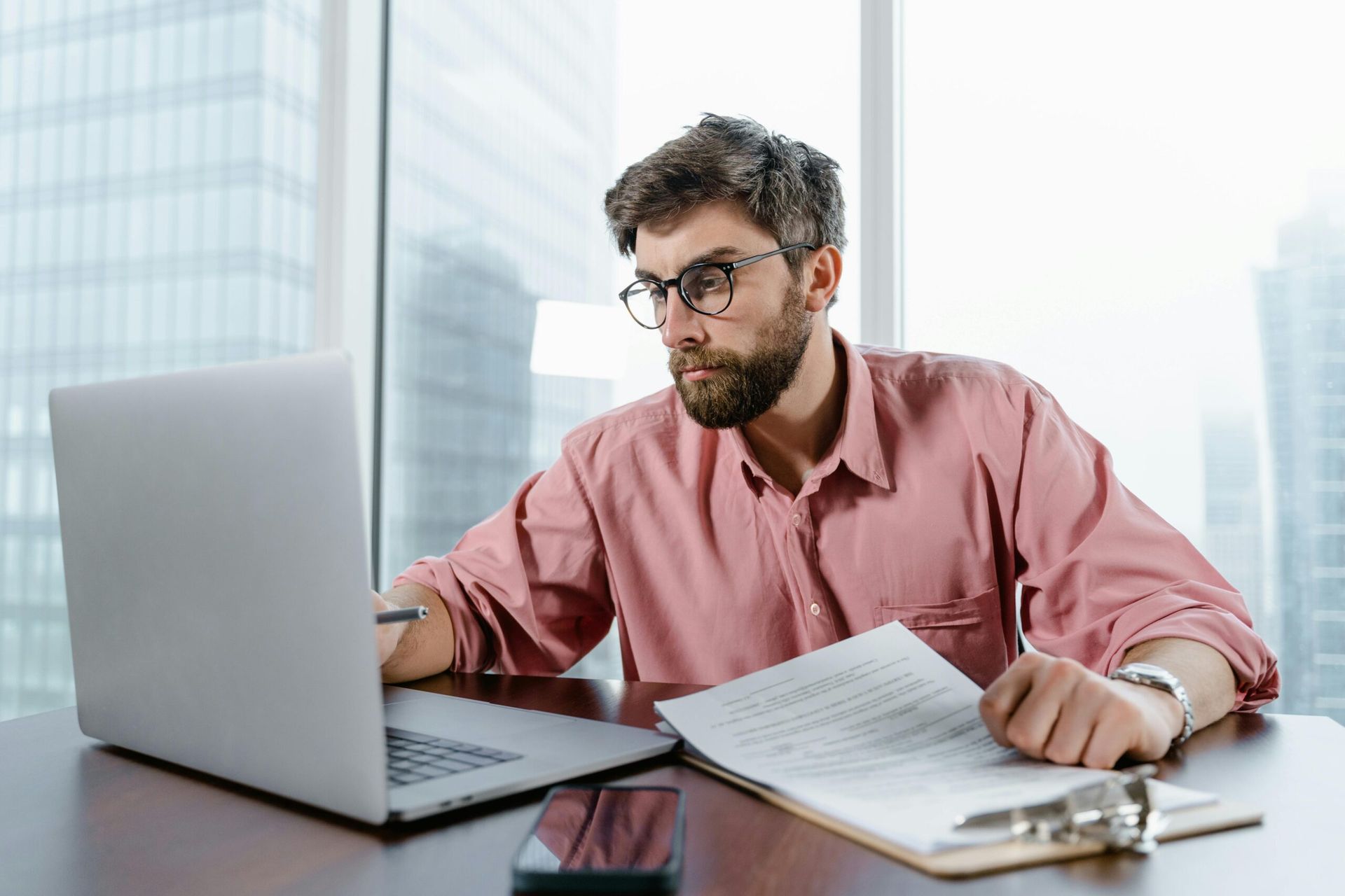 Man With Glasses and Beard Working on a Laptop, Looking at Paperwork, Indoors in a High-rise Building — Accountsloop Tax & Business Advisory in Geelong, VIC