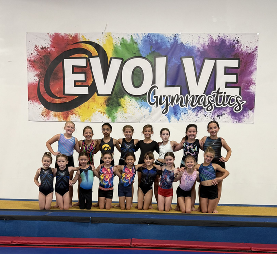 Evolve Gymnastics team posing in front of a colorful gym banner on a mat