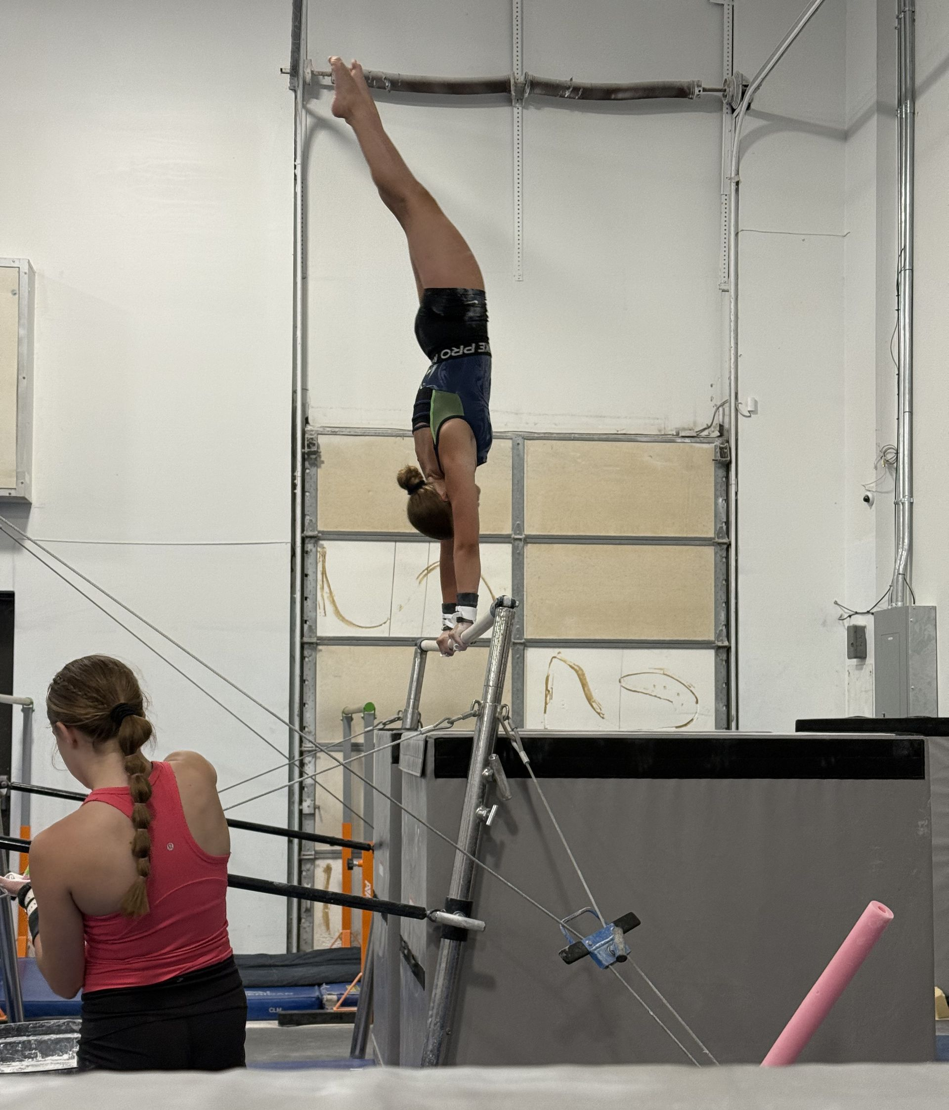 Gymnast performing a handstand on uneven bars in an indoor training gym