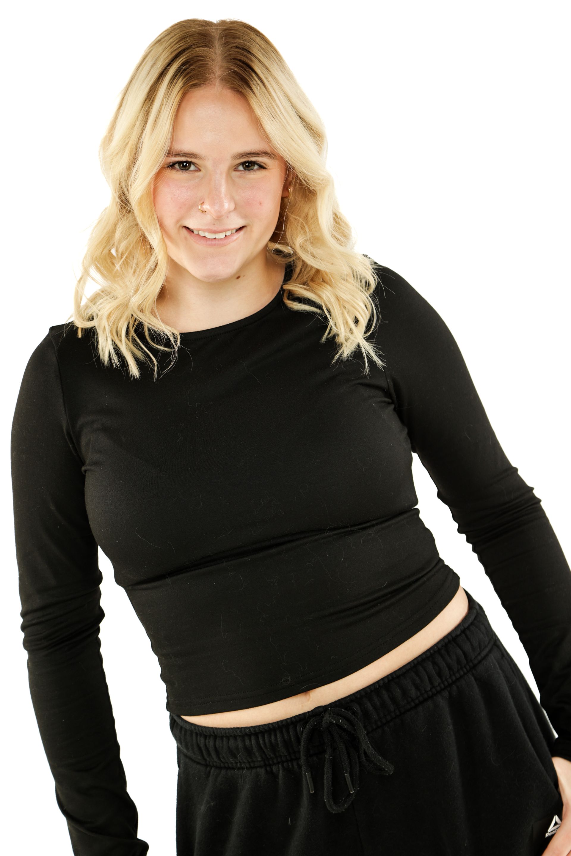 Blonde woman in a black long-sleeve top and black pants, posing against a white background.