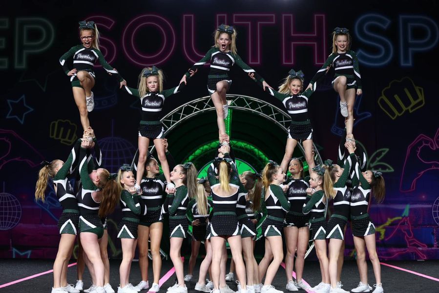 Cheerleading team in black uniforms performing a stacked stunt on stage with a purple-lit backdrop