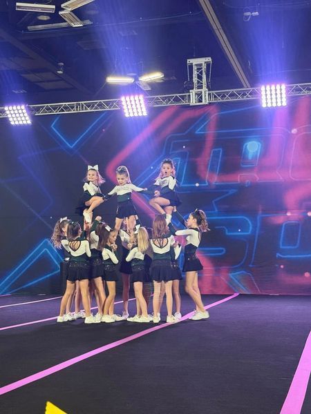 Cheerleading team posing on a stage with neon lights and a black mat