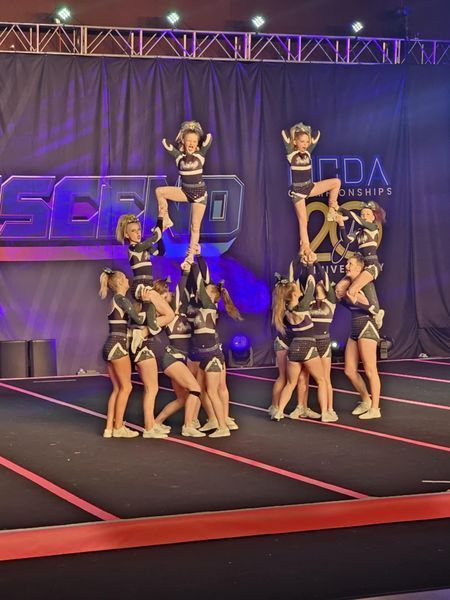 Cheer squad performing a stunt on a lit stage with purple backdrop and red floor lines