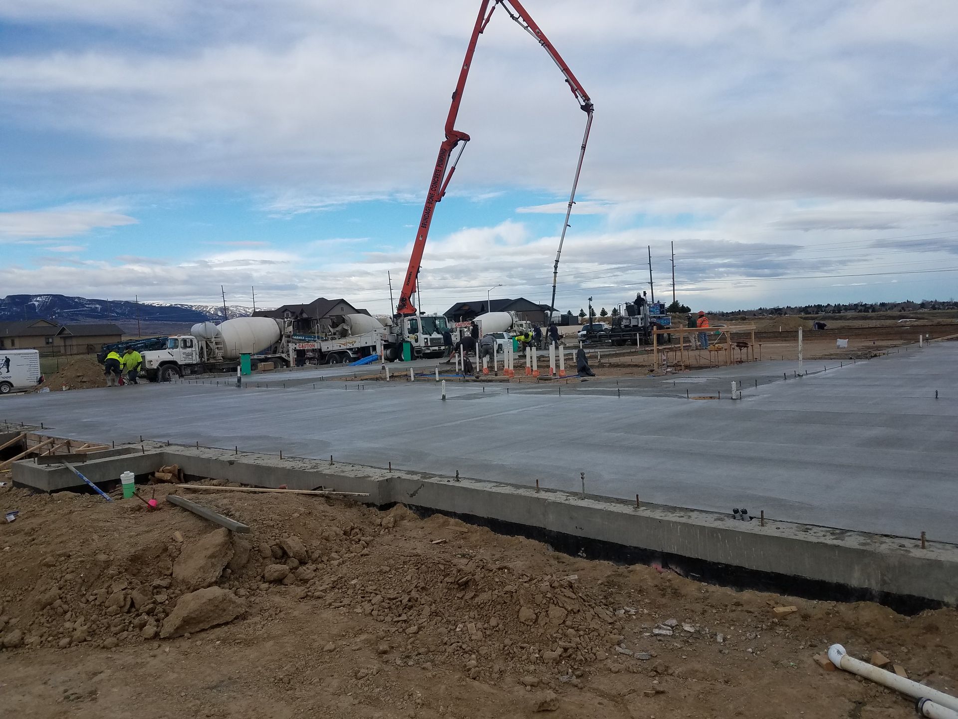 Construction site with a red concrete pump pouring over a large concrete slab under a cloudy sky