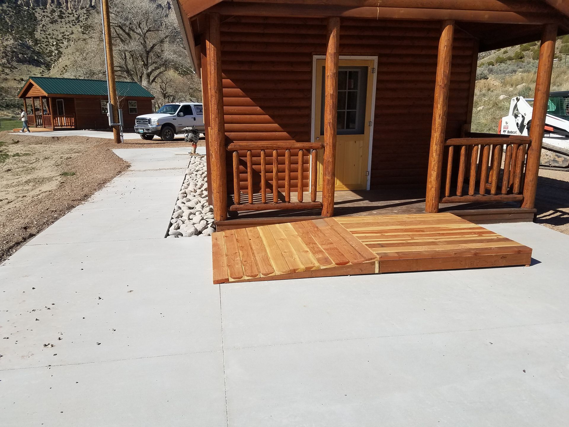 Wooden cabin porch with ramp beside a concrete path in a rustic campground setting