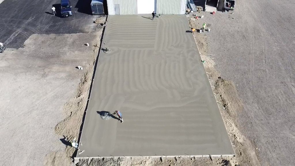 Freshly poured concrete sidewalk patch between asphalt roads, with small tools along the edge.