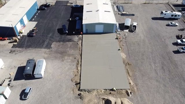 Aerial view of an industrial lot with buildings, parked vehicles, and a large concrete slab under construction.