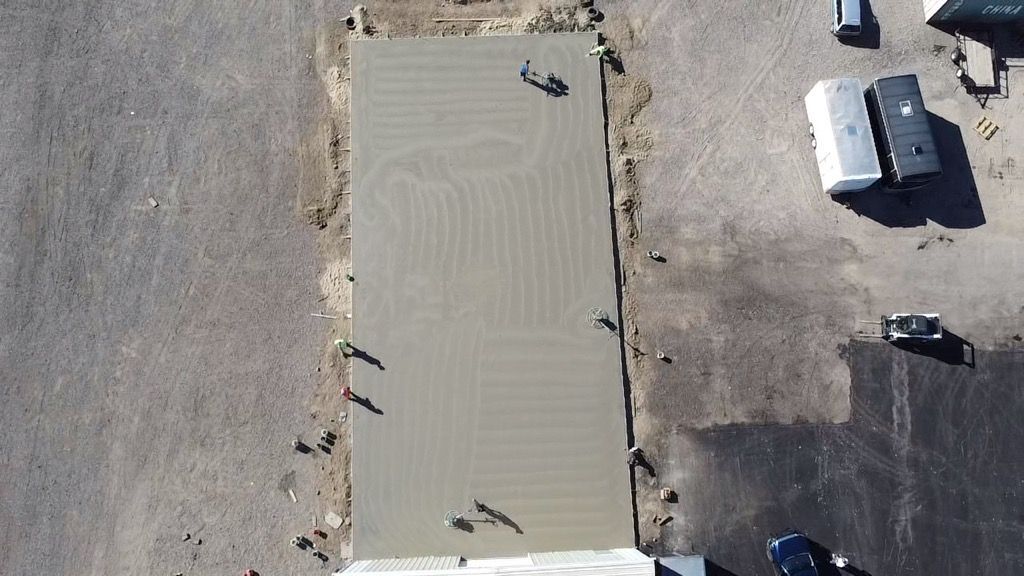 Aerial view of a large rectangular beige building roof beside a parking lot with a few vehicles.