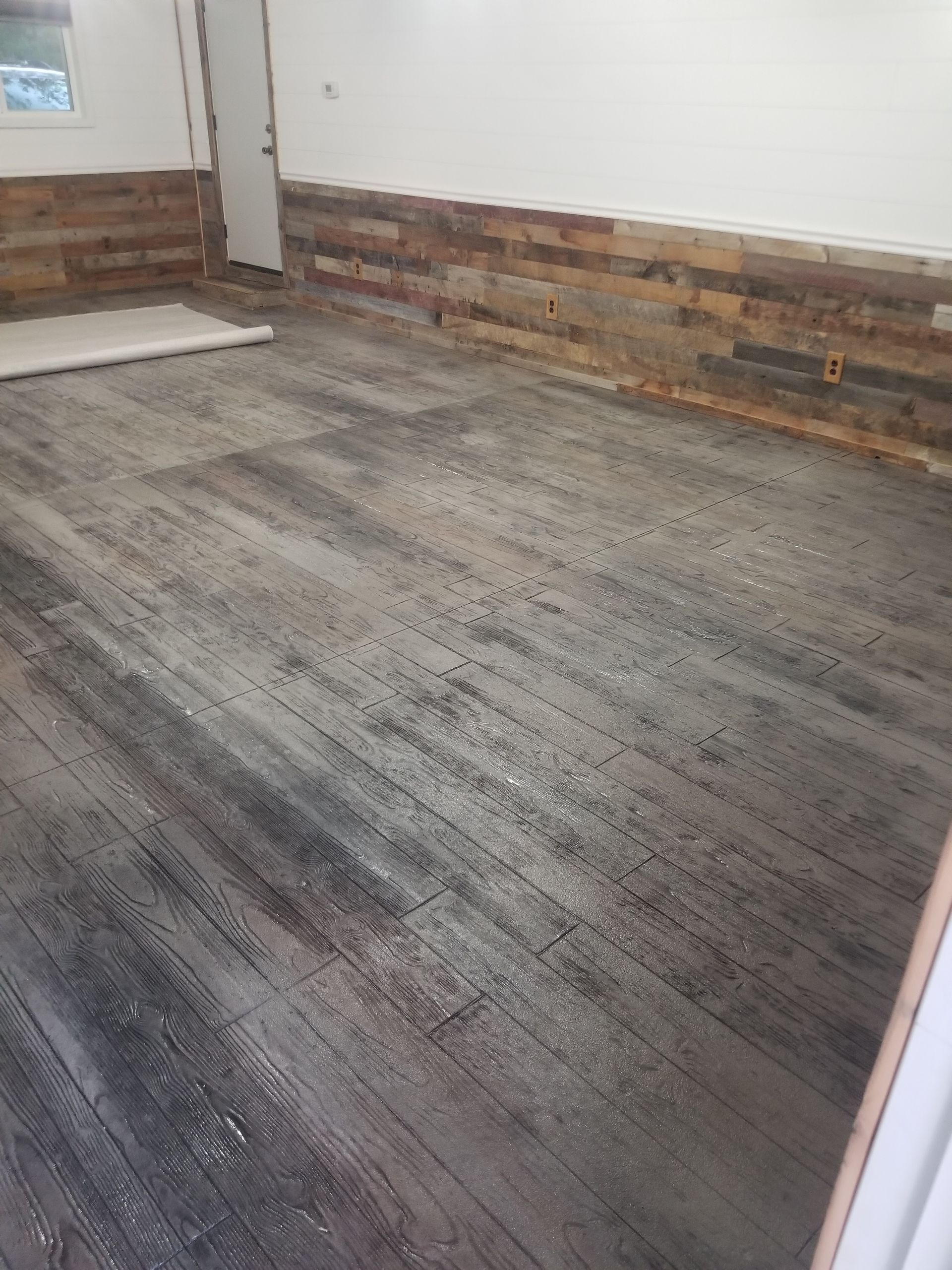 Empty room with gray flooring and exposed wood accent wall along the baseboards