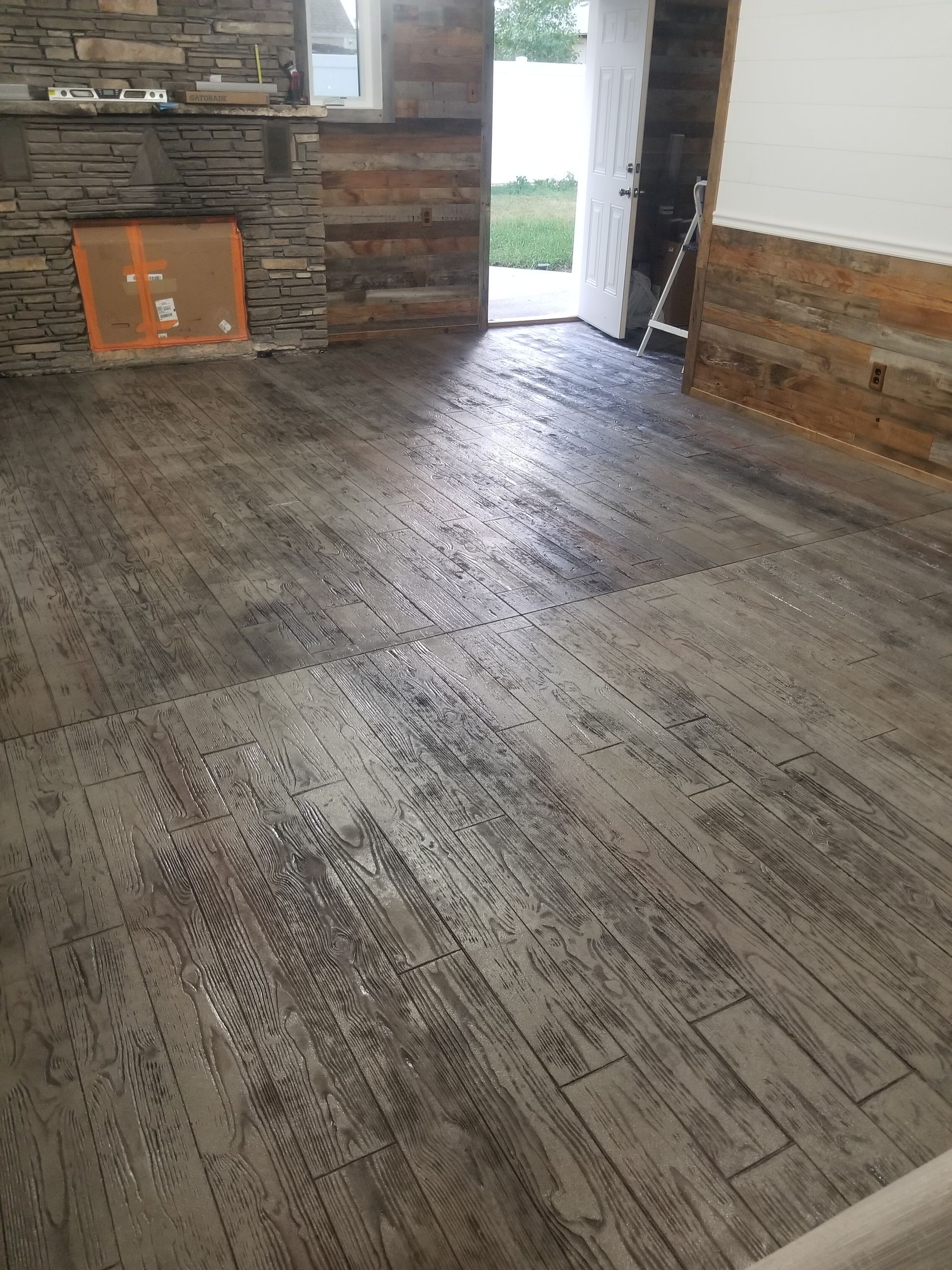 Empty rustic room with weathered wood floor, stone wall, and an open doorway to outside.