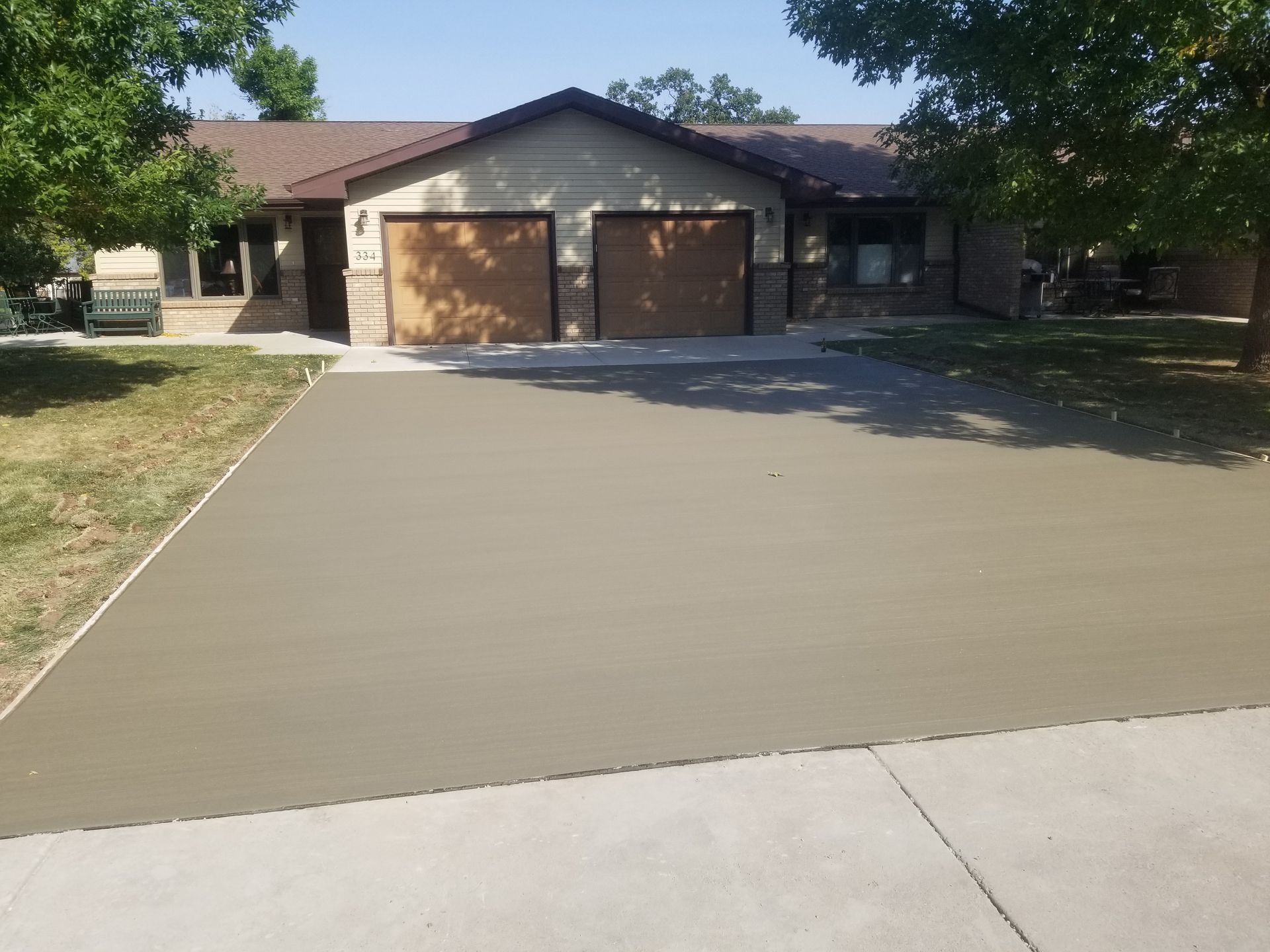Concrete driveway leading to a single-story house with a two-car garage and trees shading the front yard