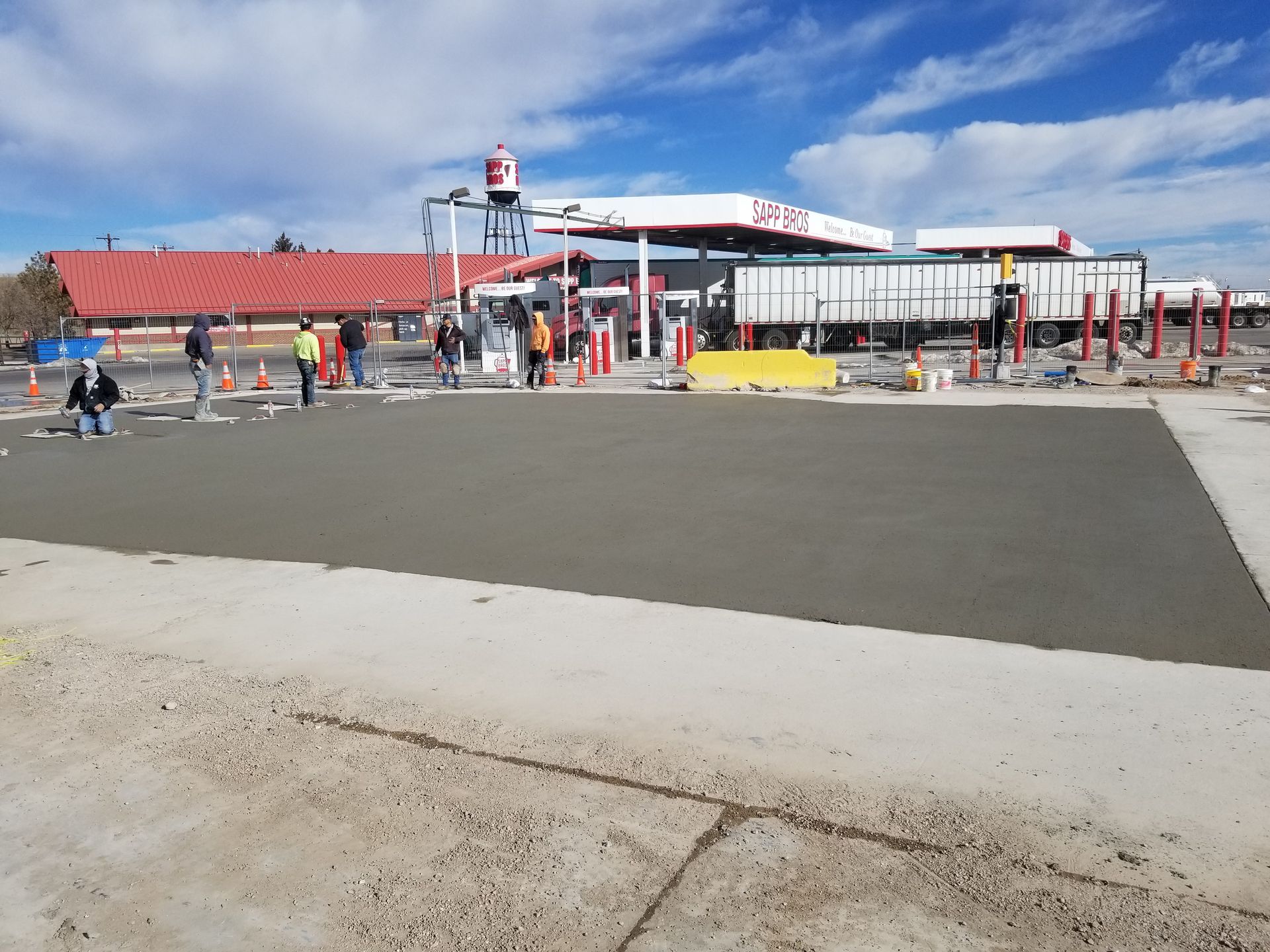 Gas station under construction with workers and barriers on a clear day