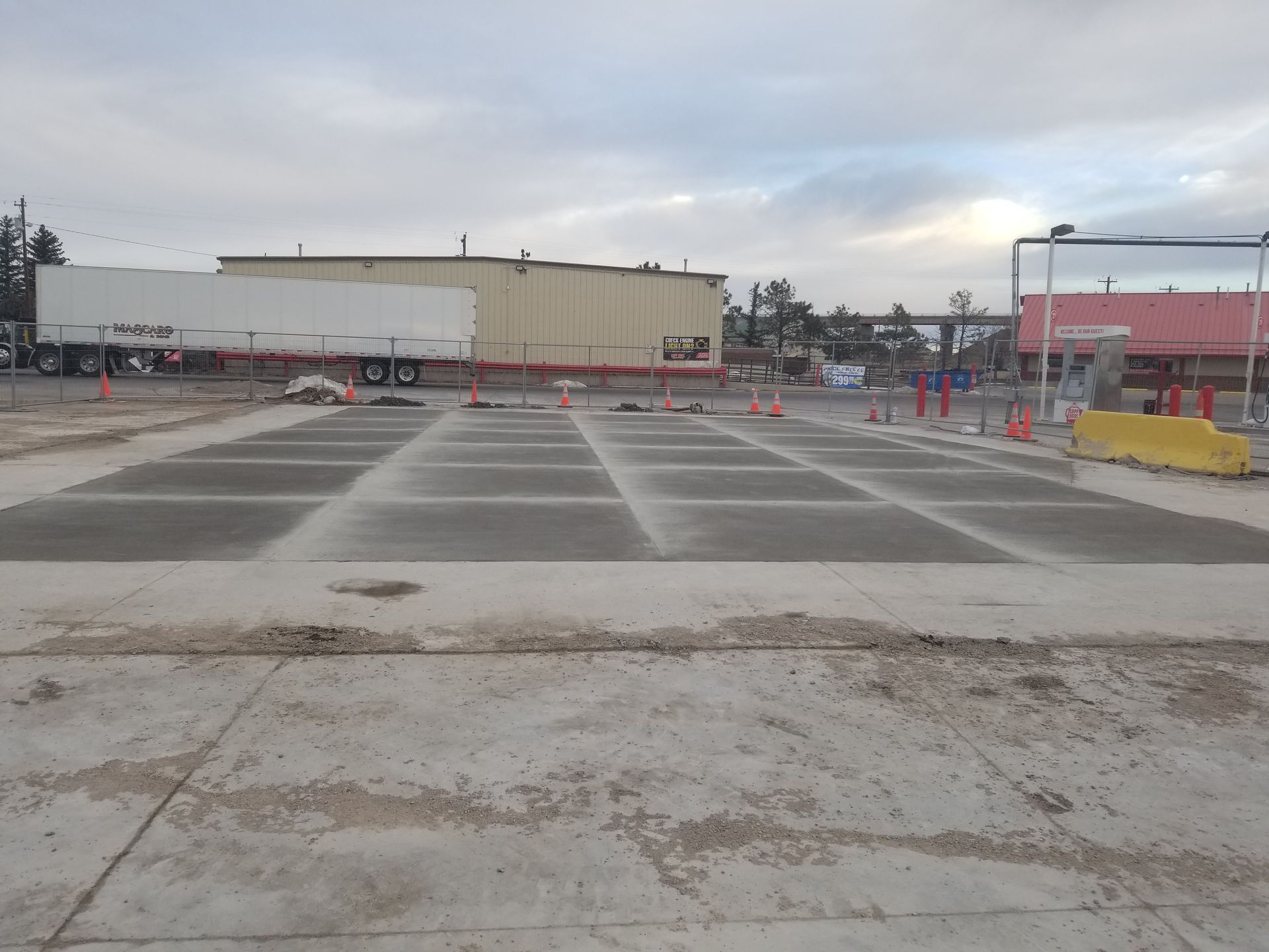 Empty parking lot with painted lanes, concrete barriers, and industrial buildings under a cloudy sky