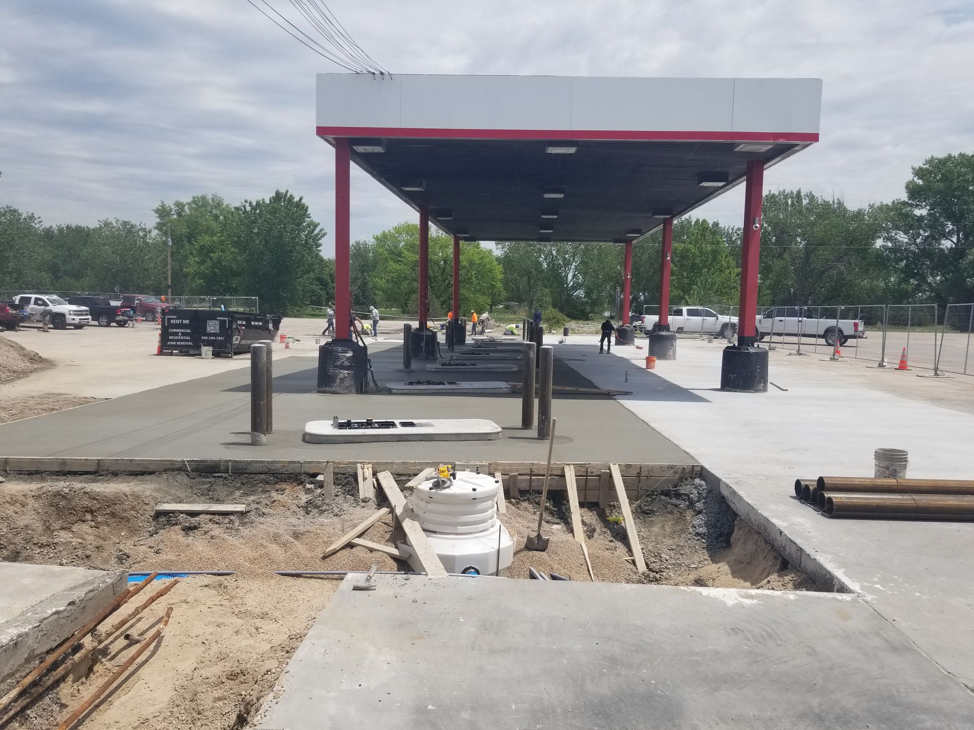 Outdoor construction site with a red-roofed canopy, concrete work area, and workers in the distance