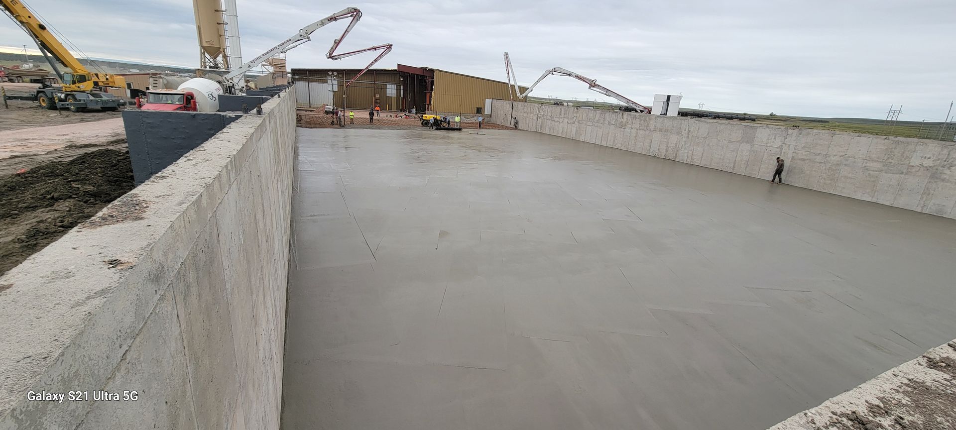 Empty concrete industrial pit with cranes and construction equipment in the background