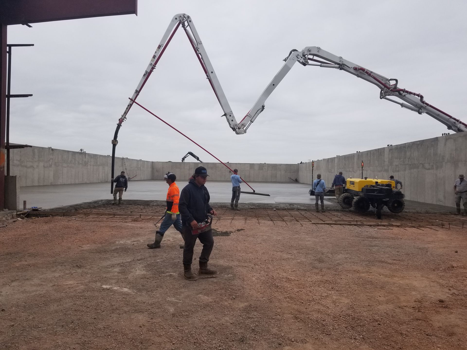 Concrete pump truck spraying concrete at a construction site, with workers nearby and high retaining walls.