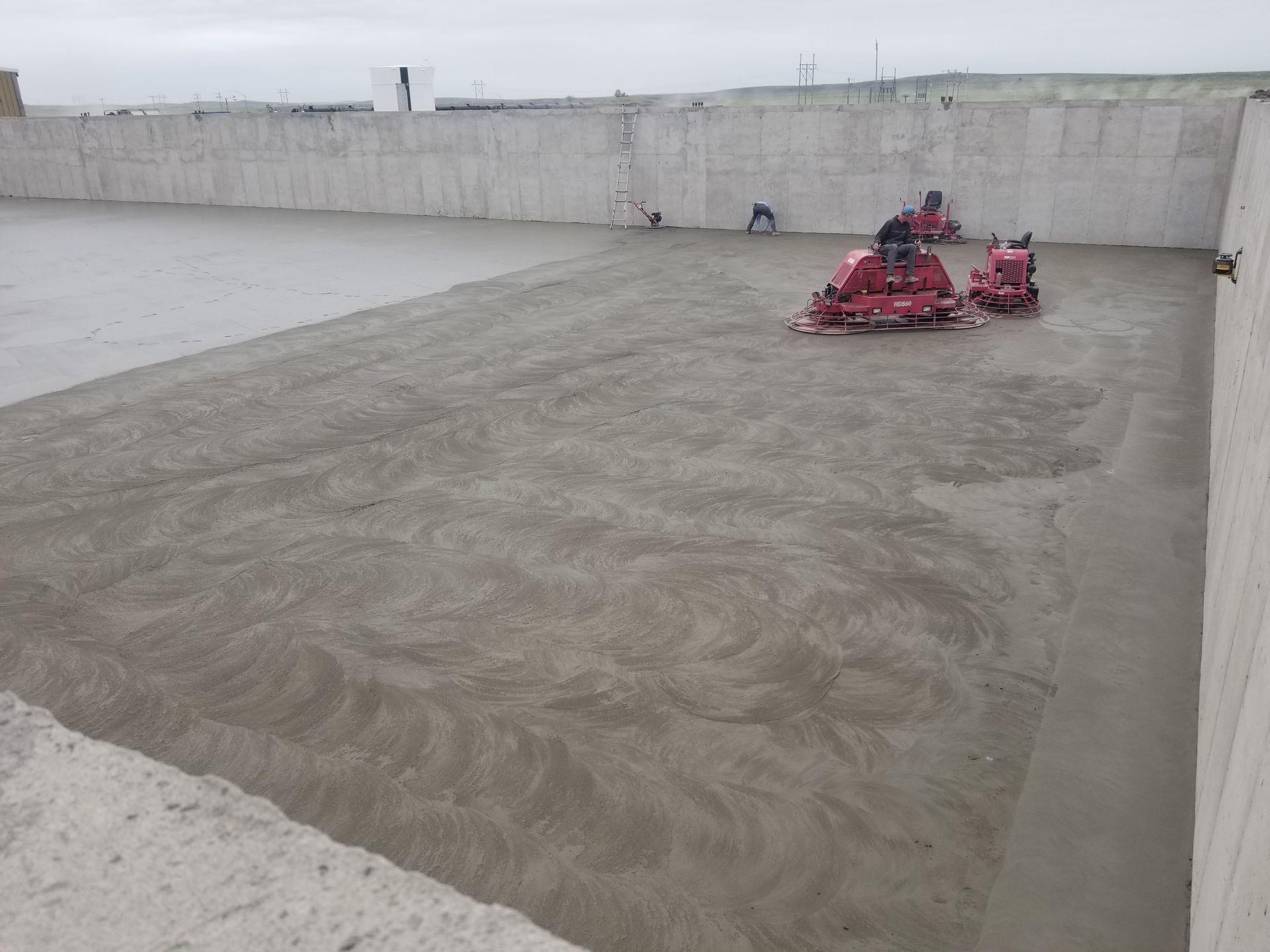Concrete slab in a construction yard with a stack of red equipment near a tall wall.