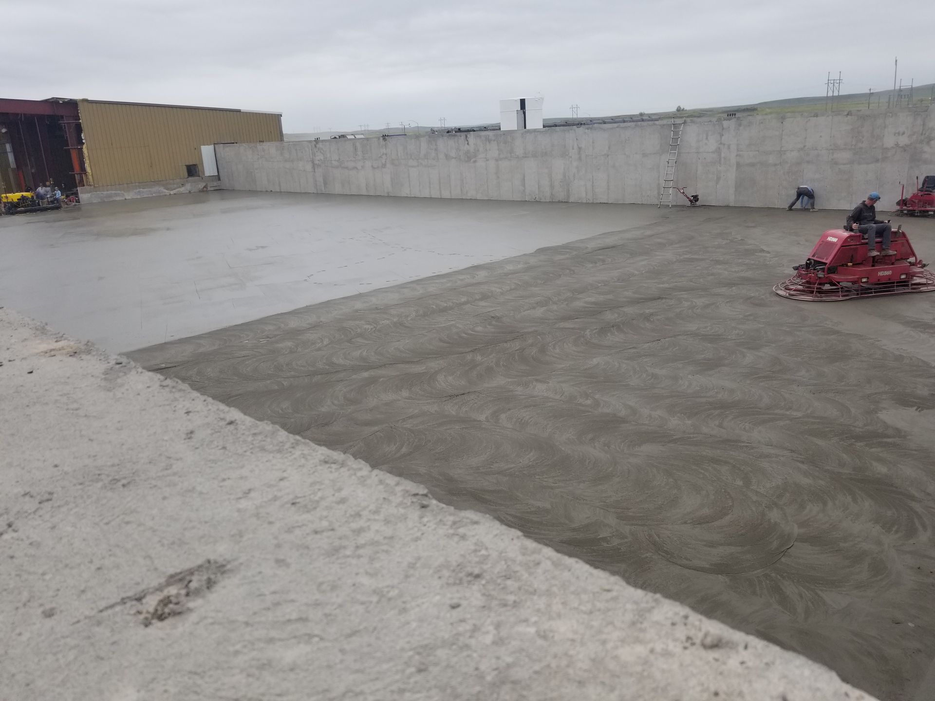 Concrete slab under construction with a worker smoothing wet concrete using a power trowel