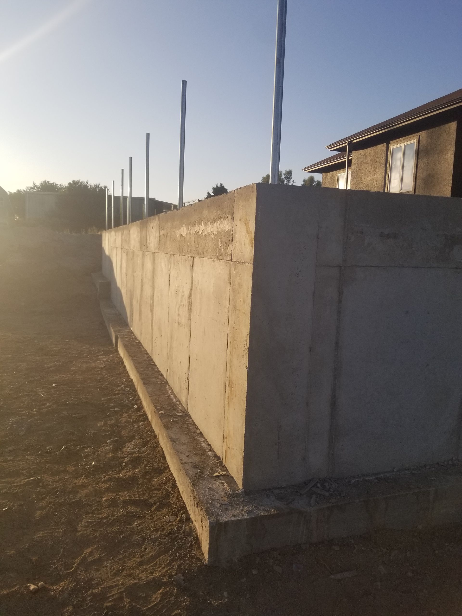 Concrete wall in a sunlit rural yard beside a small building at sunset