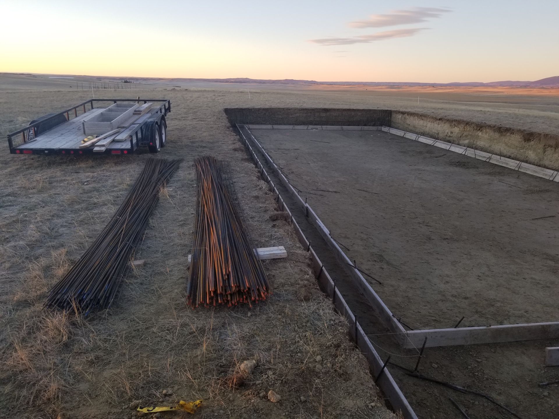 Construction materials laid out on a sandy construction site at sunset, with foundation forms in place.