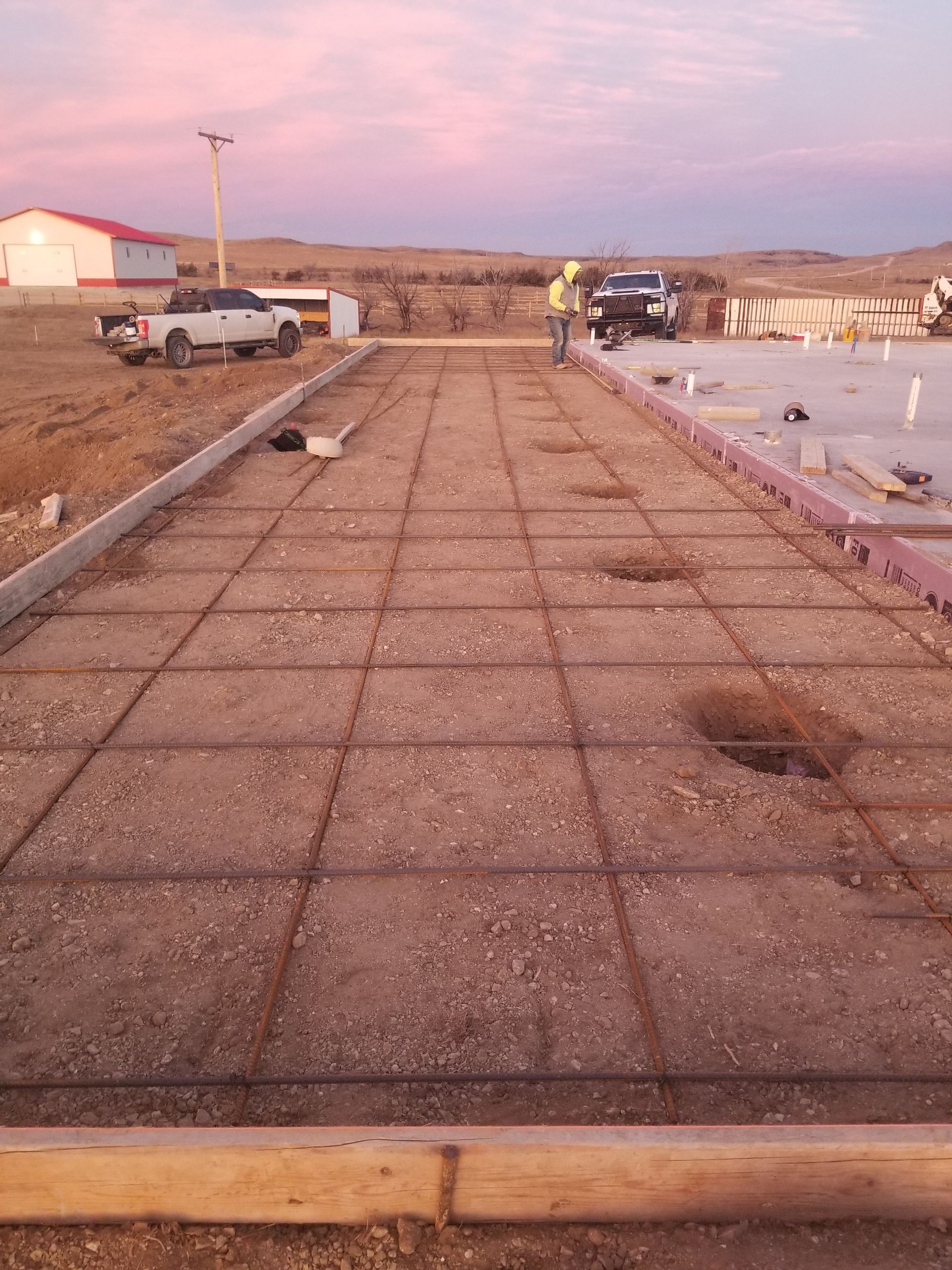 Rooftop walkway with concrete slabs, parked truck, and rows of materials at sunset.