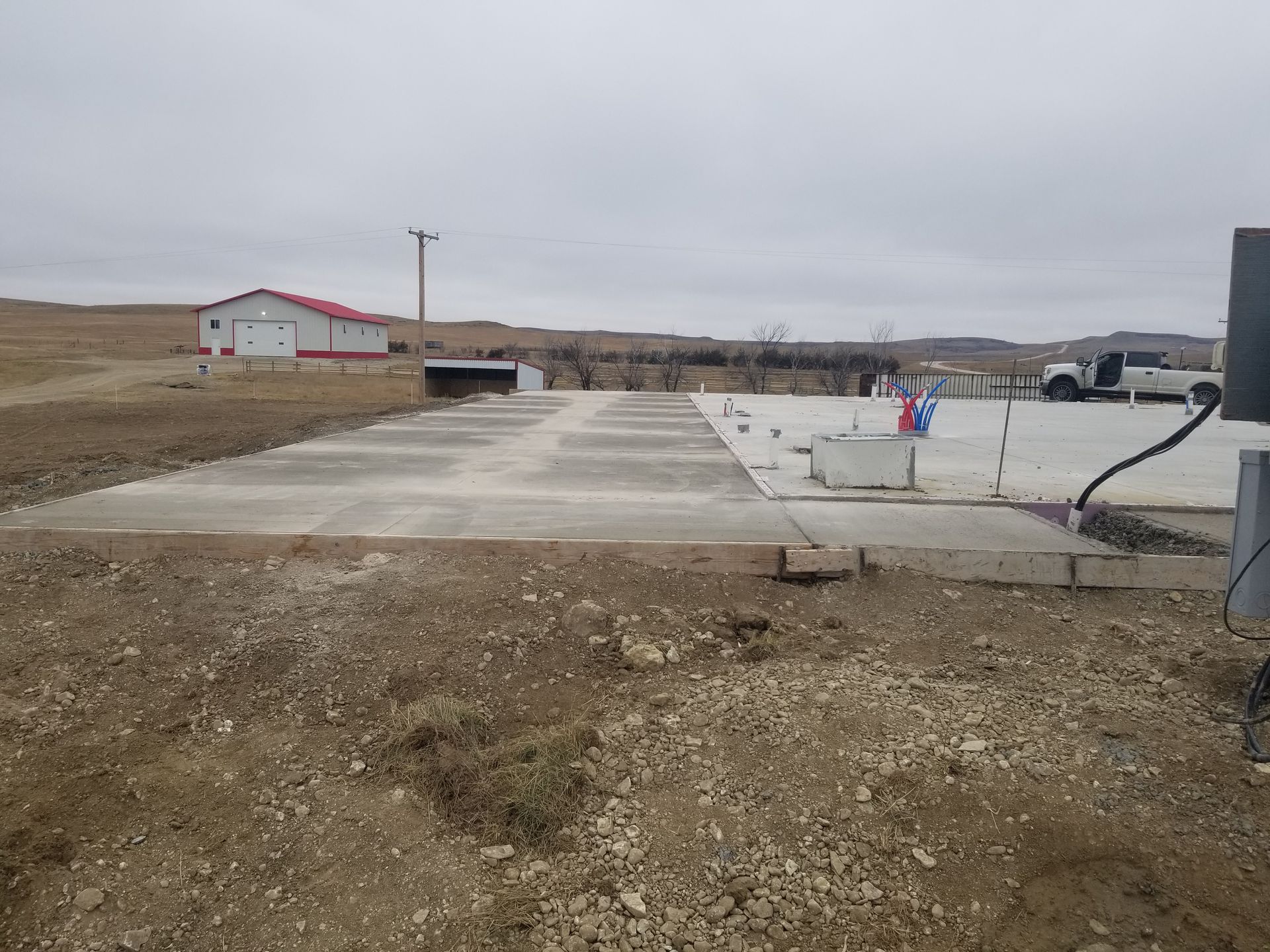 Empty concrete foundation site with dirt foreground and overcast sky