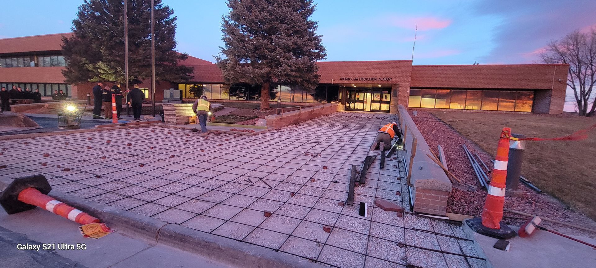 Cracked concrete parking lot with orange traffic cones beside a low building at dusk